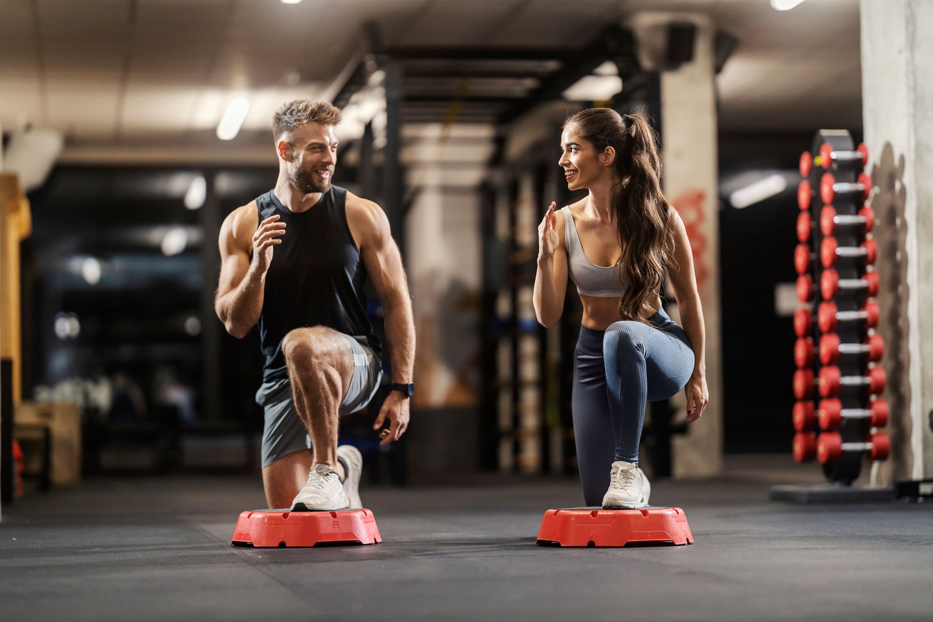 Happy muscular fit gym couple doing lunges exercises on stepper at 