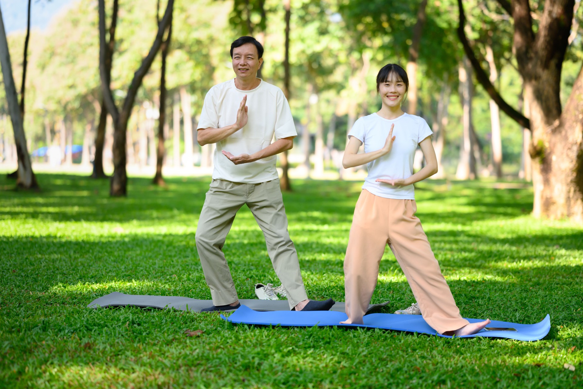 Glücklicher älterer Mann und seine Tochter machen Qigong-Übungen im Park. Konzept für psychische Gesundheit und Familienaktivitäten