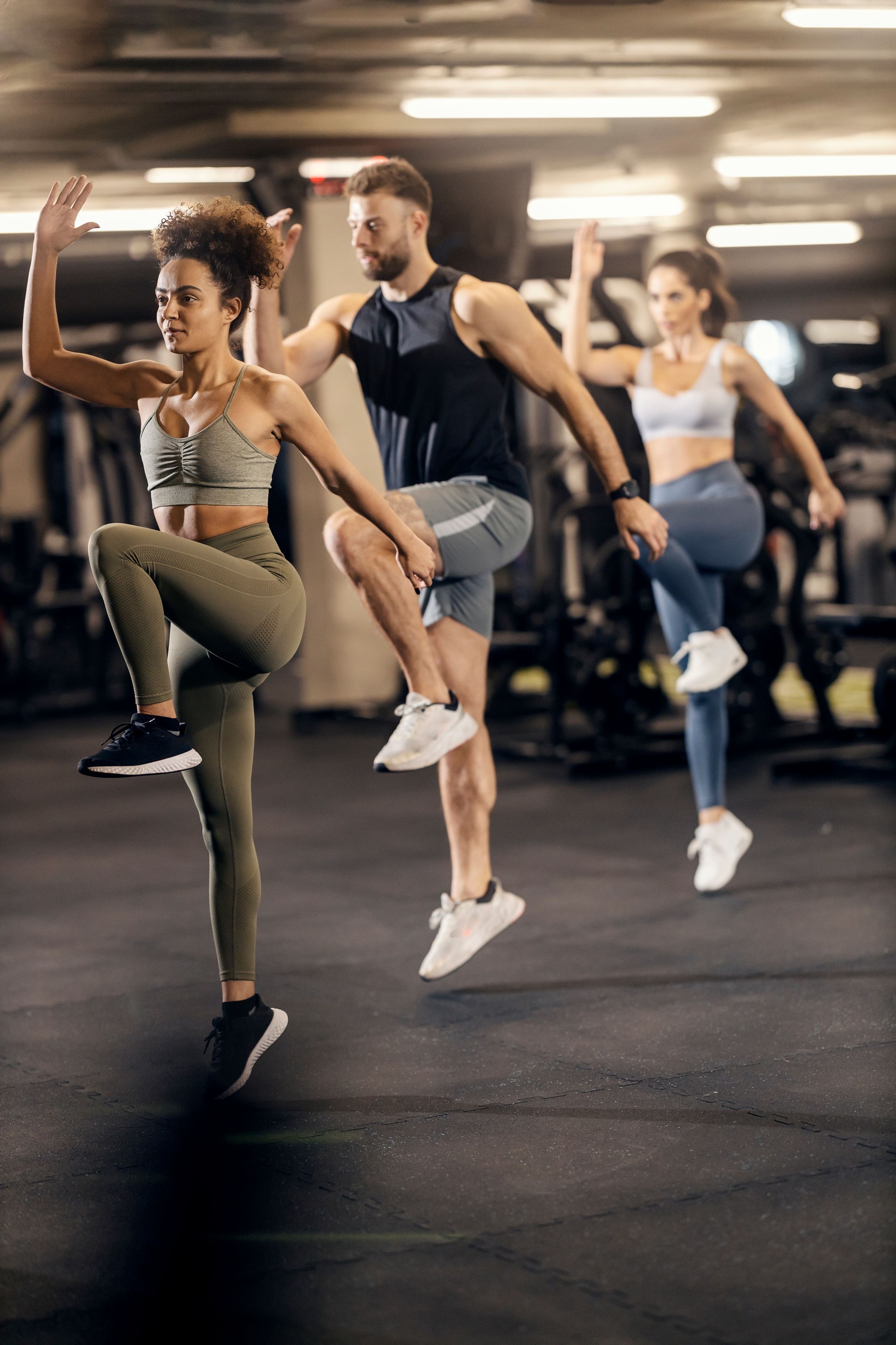 Full length shot of sportspeople in shape doing jumping exercises in a gym.